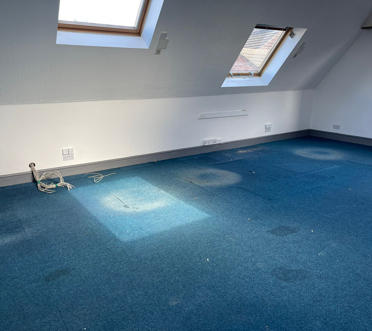 run down office space with old blue carpet, white walls and skylights on the sloped back wall