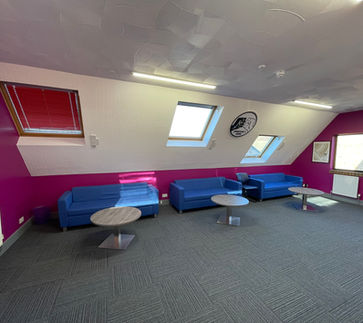 Refurbished space with grey carpets, fresh wall paint white and fuchsia, 3 blue sofas and round, silver coffee tables, with skylights on the sloped back wall