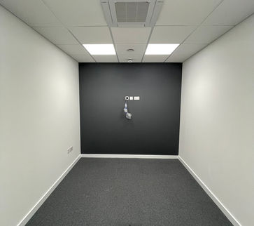 Empty newly refurbished room with grey floor, white walls and white ceilings with square ceiling lights and wires sticking out the back wall