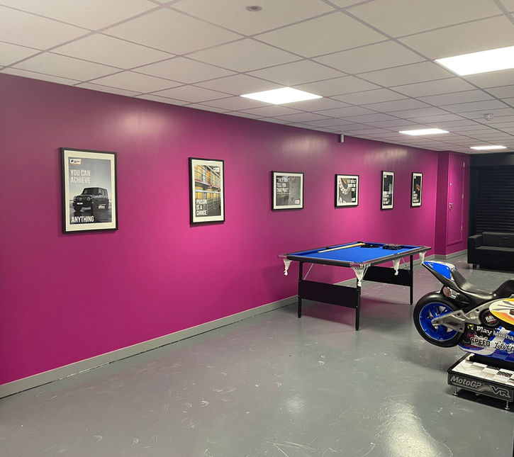 Refurbished end of corridor with one fuchsia wall with artwork on, several arcade games and a pool table