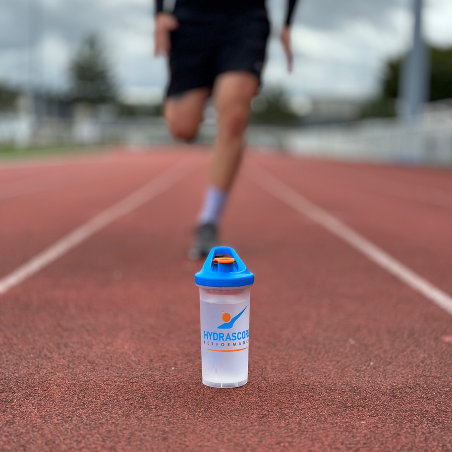 shaker hydrascore 700ml avec mélangeur intégré pour boisson protéinée sur une piste d'athlétisme