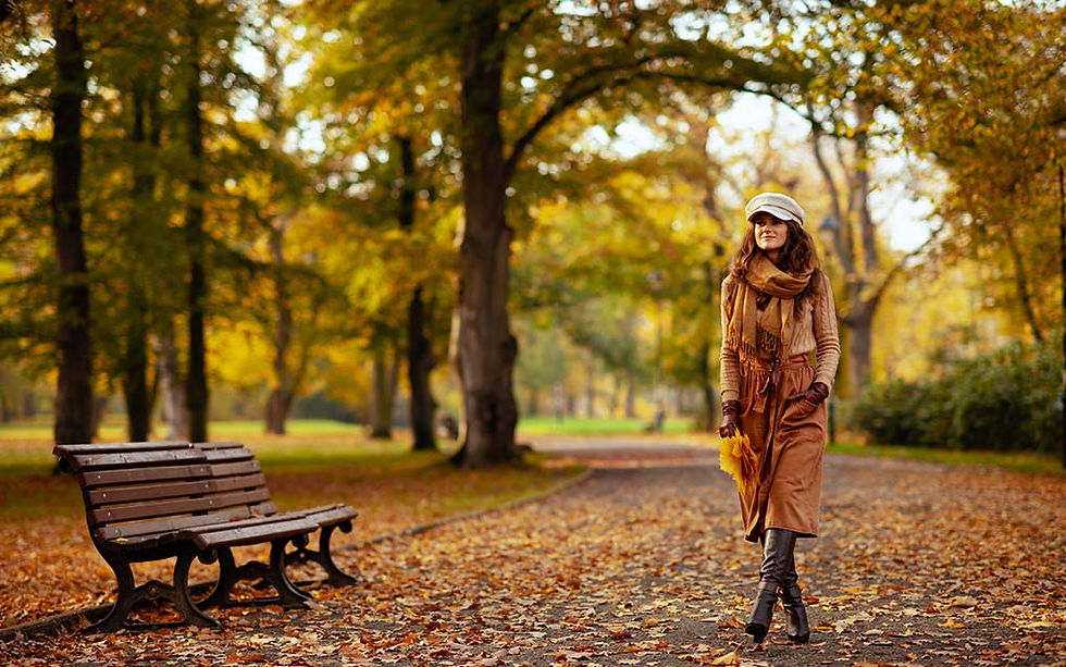 Woman walking through a park on an autumn day, surrounded by golden leaves, reflecting the calming effects of seasonal routines on mental health.