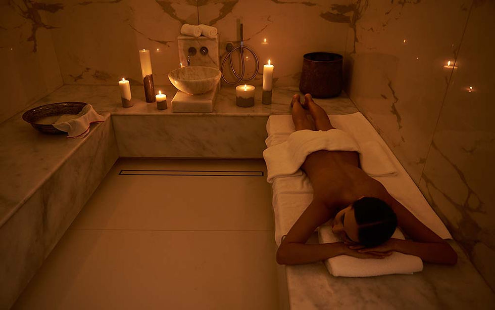 A woman lies on a marble table in a dimly lit hammam surrounded by glowing candles, evoking the soothing and purifying atmosphere of a traditional Turkish bath.