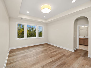 Empty room with hardwood floors, windows, and arched entry to bathroom