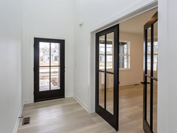 Hallway with light floor, white walls, and black French doors