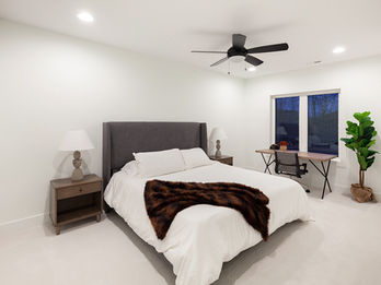 Clean, modern bedroom with bed, nightstand, desk, and plant