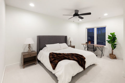 Clean, modern bedroom with bed, nightstand, desk, and plant