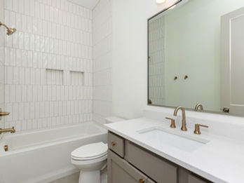 Bathroom with white tub, toilet, vanity, brass fixtures.