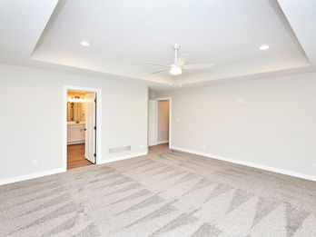 Empty bedroom with tray ceiling and open bathroom door