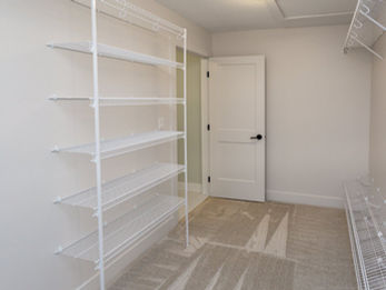 Empty walk-in closet with white shelves and door
