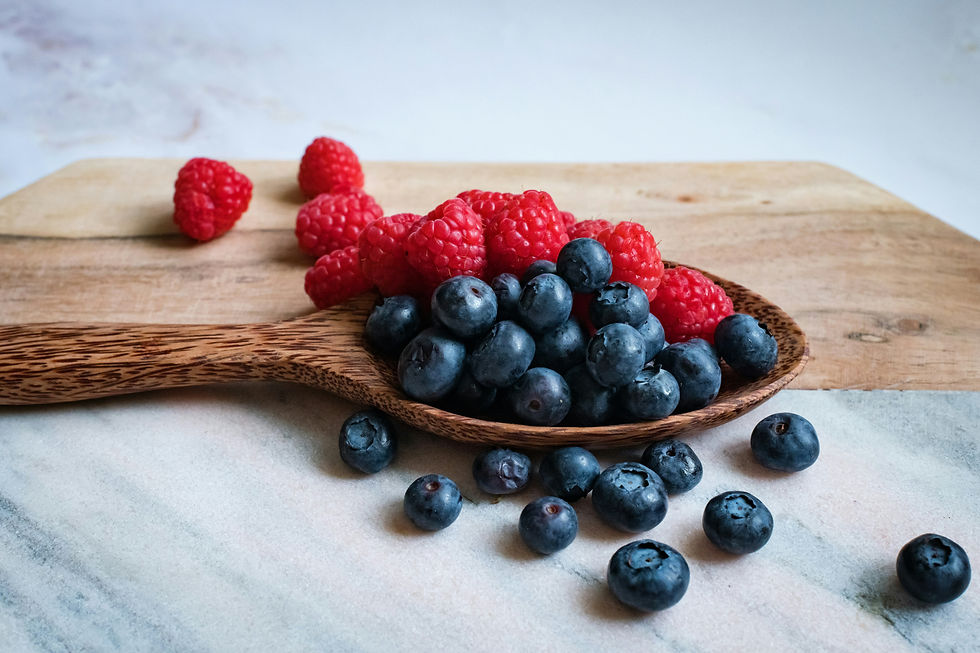 Blueberries and raspberries on a wooden spoon and cutting board on a marble surface.