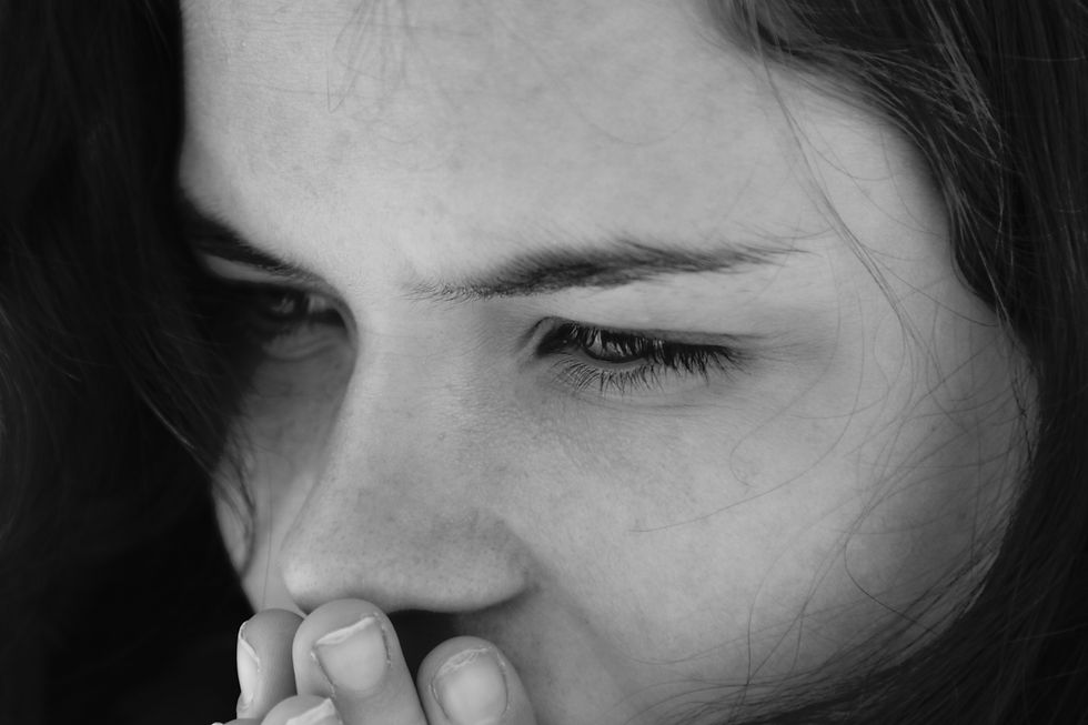 Close-up of a person in black and white, appearing pensive, with hands near mouth. Hair partially covers face.