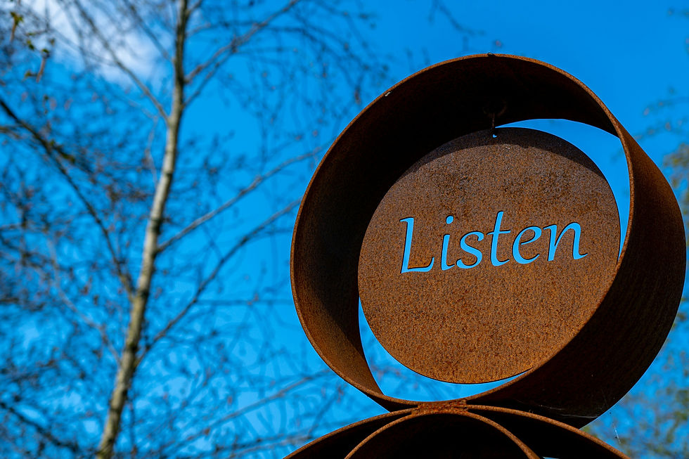 Rustic metal sculpture with the word "Listen" set against a clear blue sky and bare tree branches. Calm and reflective mood.