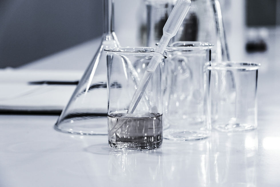 Clear glass lab beakers and pipette on a white table in a laboratory setting. Reflective surfaces create a clean, sterile mood.