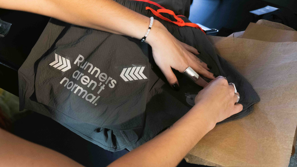 Close-up of hands applying reflective vinyl on a running New Balance t-shirt that reads “Runners aren’t normal.”