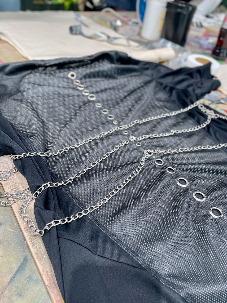 Close-up of a black upcycled adidas mesh jersey laid flat, customized with silver chains and metal eyelets.