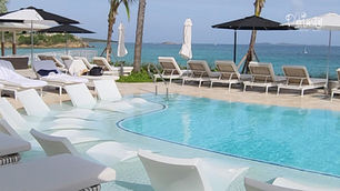 Swimming pool with curved white in-water loungers, umbrellas and an ocean view at Buoy Haus, St. Thomas.