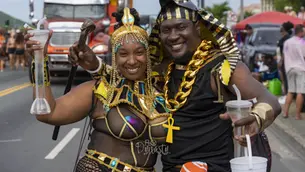 Two smiling participants in matching gold-and-black costumes pose on the road during St. Thomas Carnival 2026 J'ouvert, with a music truck behind them.