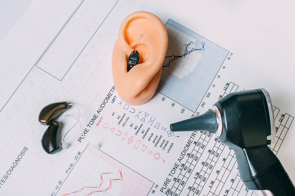 Model ear with a hearing aid, two hearing devices, and an otoscope on an audiometry chart with graphs and text, emphasizing hearing tests.