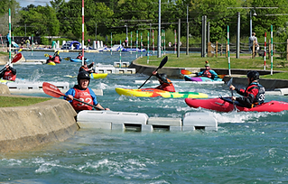 A few people in multicoloured kayaks trying out their skills on the rapids while a raft guide watches over them.