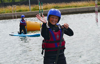 Girl, smiling and waving, dressed in a wetsuit and bouyancy aid