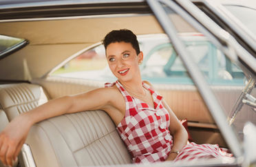 Pin-up model behind the wheel of a classic car with tan leather interior