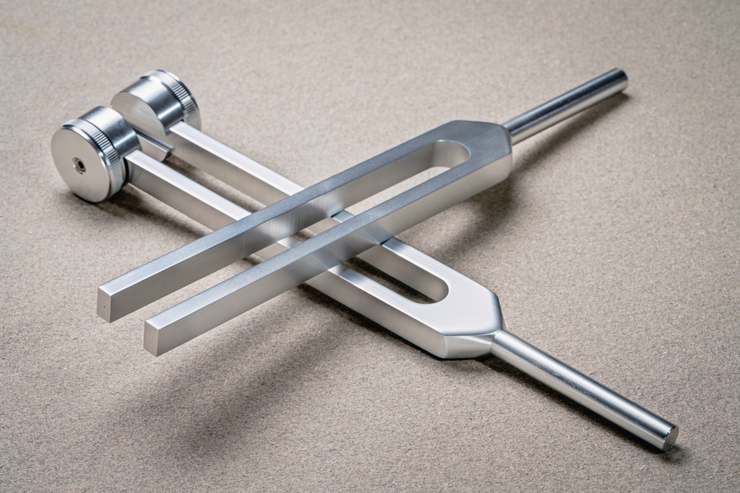 A silver tuning fork vibrating just above a water surface creating perfect geometric ripples.