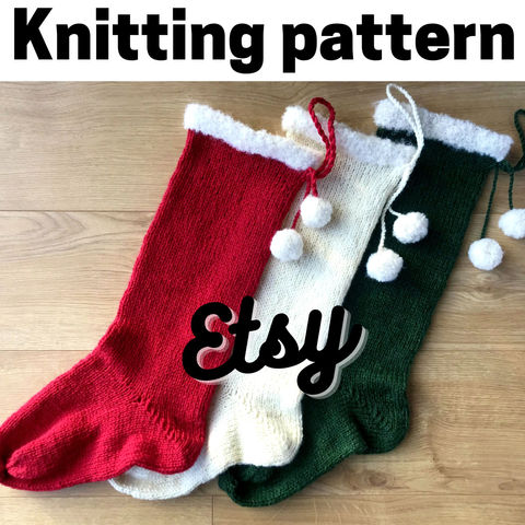 3 knit Christmas stockings (1 red, 1 cream, 1 green) with cream fluffy cuffs and pompoms, lying on a wooden surface