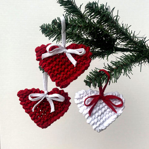 Red and white chunky knit hearts with contrasting bows hanging on a Christmas tree
