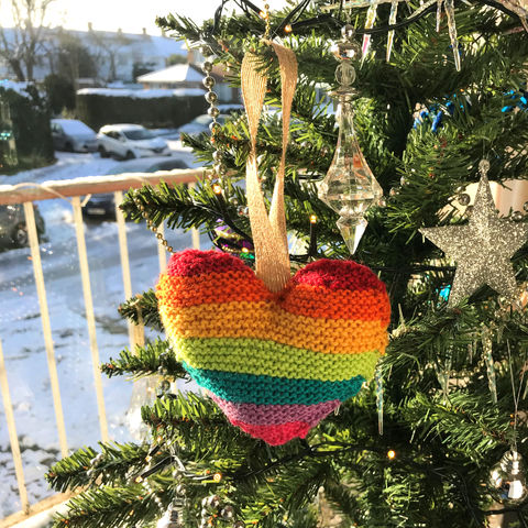 Rainbow striped hand knit stuffed wool heart hanging on a Christmas tree