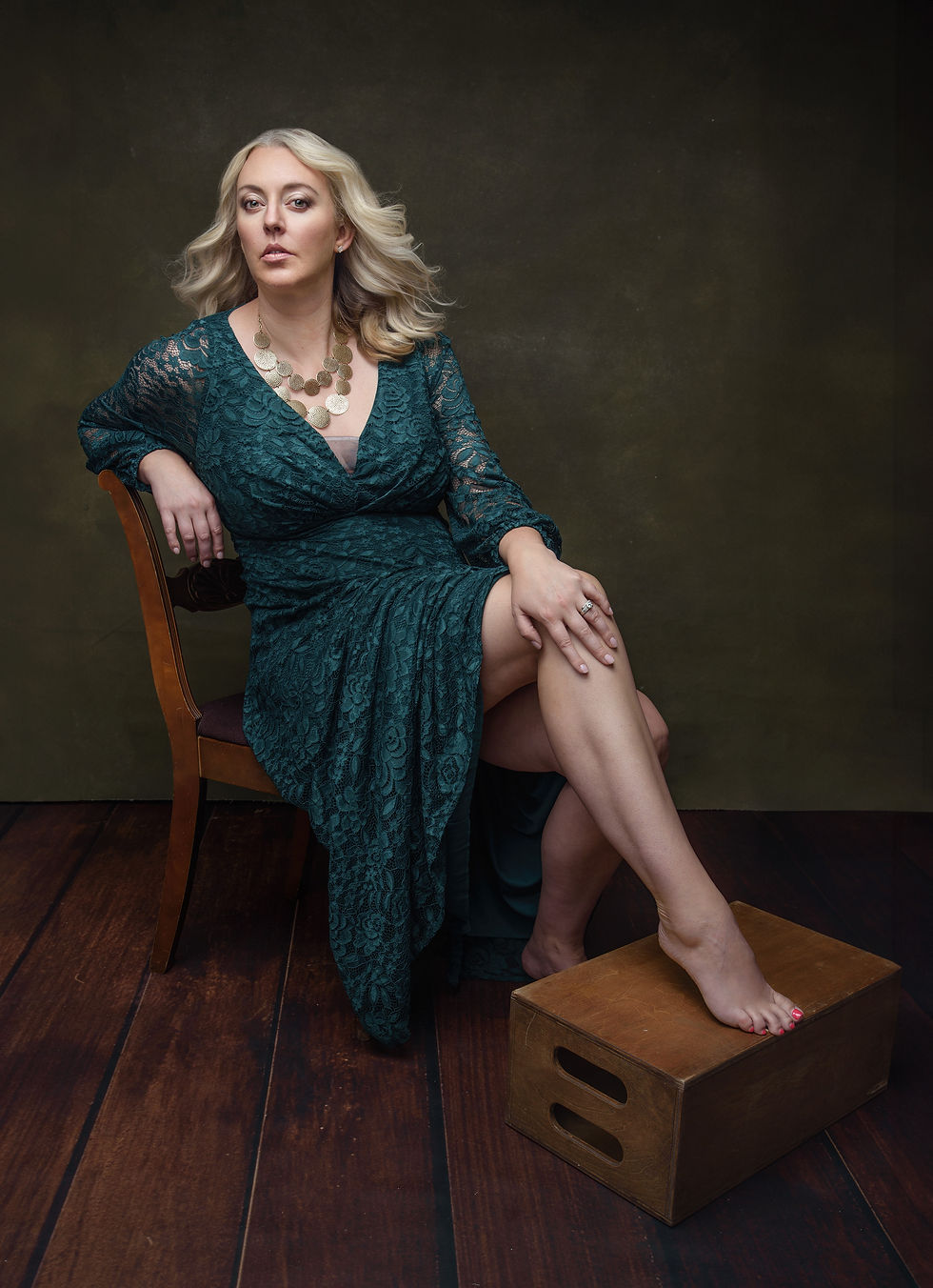 Woman wearing green lace dress sitting on a chair.