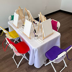 Kids table with mini easels, and mini aprons laid on kids chairs.