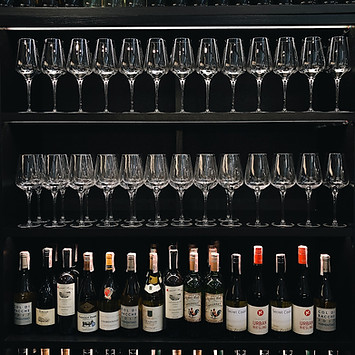 A visually pleasing wine shelf with orderly rows of wine glasses and neatly arranged wine bottles. The photo captures the organized display, showcasing the elegance and sophistication of a well-curated wine collection.