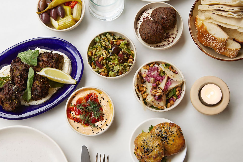 Assorted Mediterranean dishes on a white table: falafel, hummus, olives, flatbread, and a lit candle creating a cozy dining vibe.