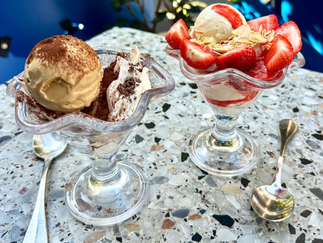 Two dessert glasses on a terrazzo table, one with tiramisu and the other with strawberries and vanilla ice cream, silver spoons beside them.