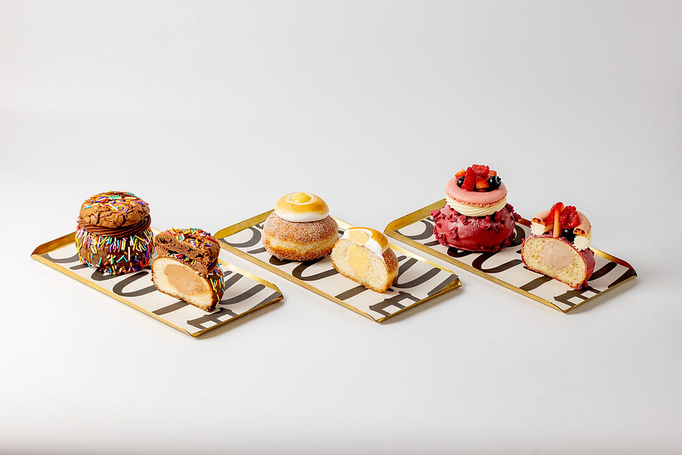 Three donuts on trays: a chocolate sprinkle bomb, a lemon meringue donut, and a berry macaron. Minimalist white background.