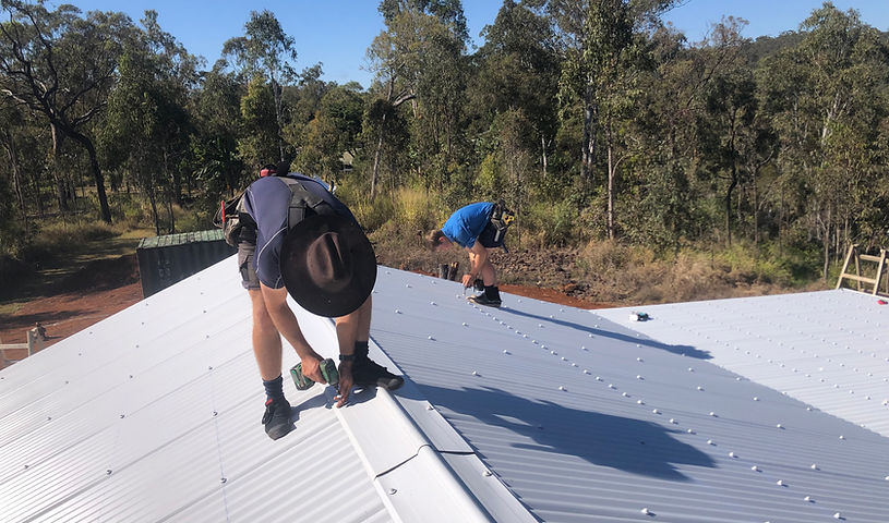 Two roofing carpenters installing a white colourbond roof in the bush
