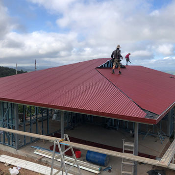 Two roofers installing a red roof silhouetted against an overcast skyline