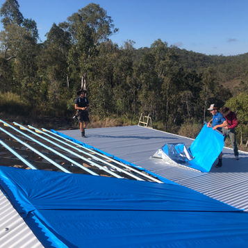 Roofers installing insulation and colourbond roofing overlooking the bush