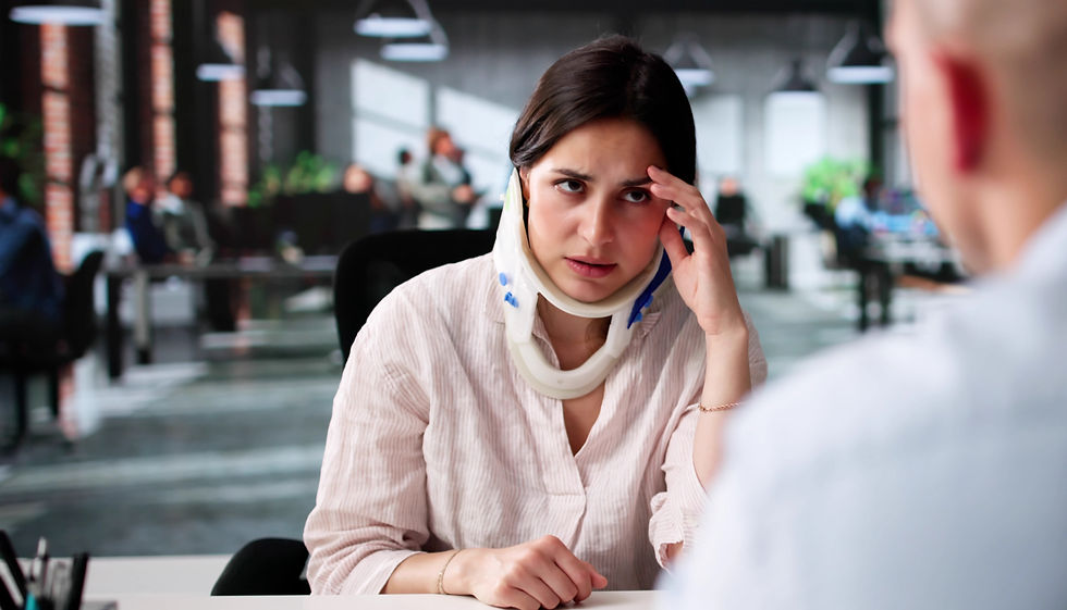 Woman in a neck brace looks concerned in an office, holding her forehead. Blurred background with people working and hanging lights.