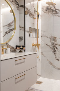 Marmoria ja messinkiä yhdistävä kylpyhuone, jossa pehmeä valo korostaa ylellisyyttä ja rauhaa.