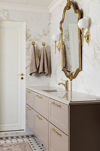 Kultakehyksinen peili ja klassinen valaisin marmoriseinää vasten.