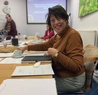 A smiling woman sat at a table with other people reading documents