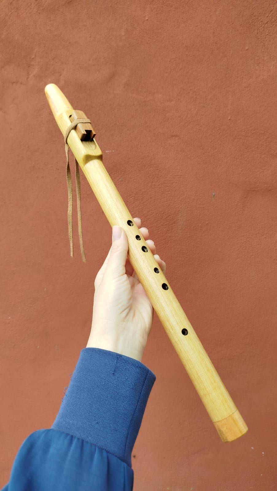 Flauta nativa de madera, sostenida por una mano.