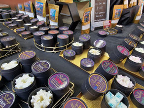 Shelley's Waxmelts market stall — colourful wax melts in cardboard jars displayed on black cloth with gold trays