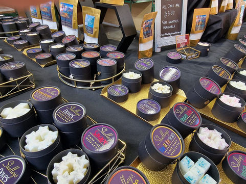 Shelley's Waxmelts market stall — colourful wax melts in cardboard jars displayed on black cloth with gold trays