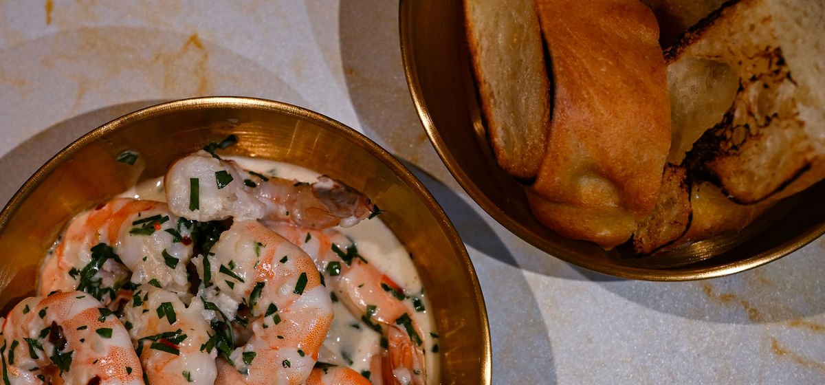 Garlic butter shrimp in a gold bowl beside warm focaccia