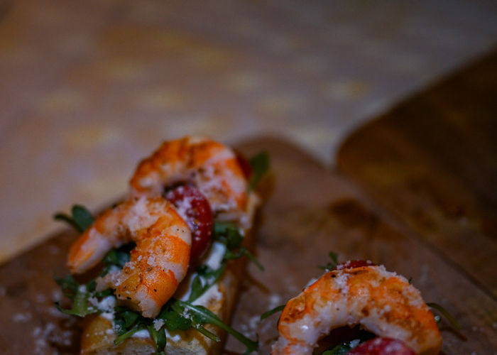 Zesty shrimps bruschetta on a wooden board with ricotta and arugula