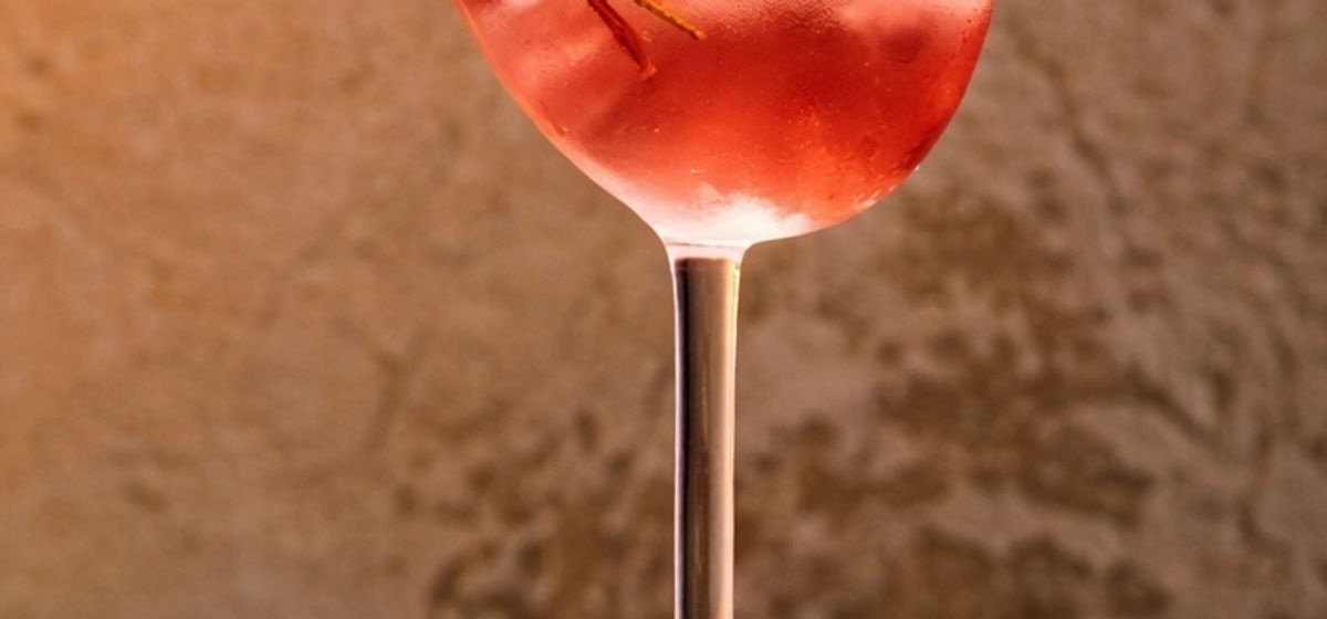 Signature pink prosecco cocktail in a bird-shaped coupe glass on marble