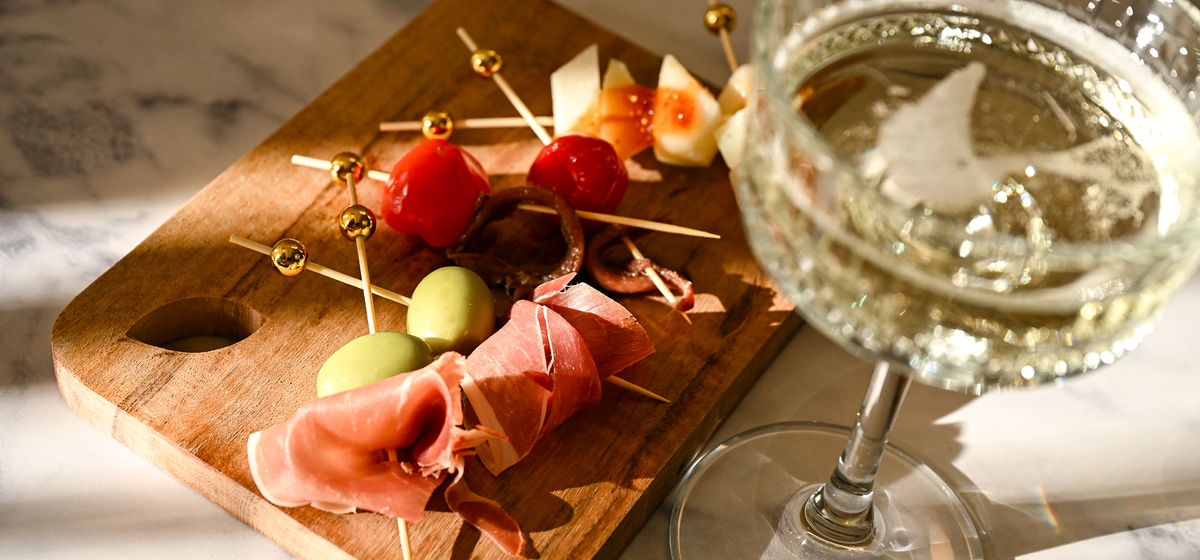 Basque pintxos trio with prosciutto, olives and prosecco glass